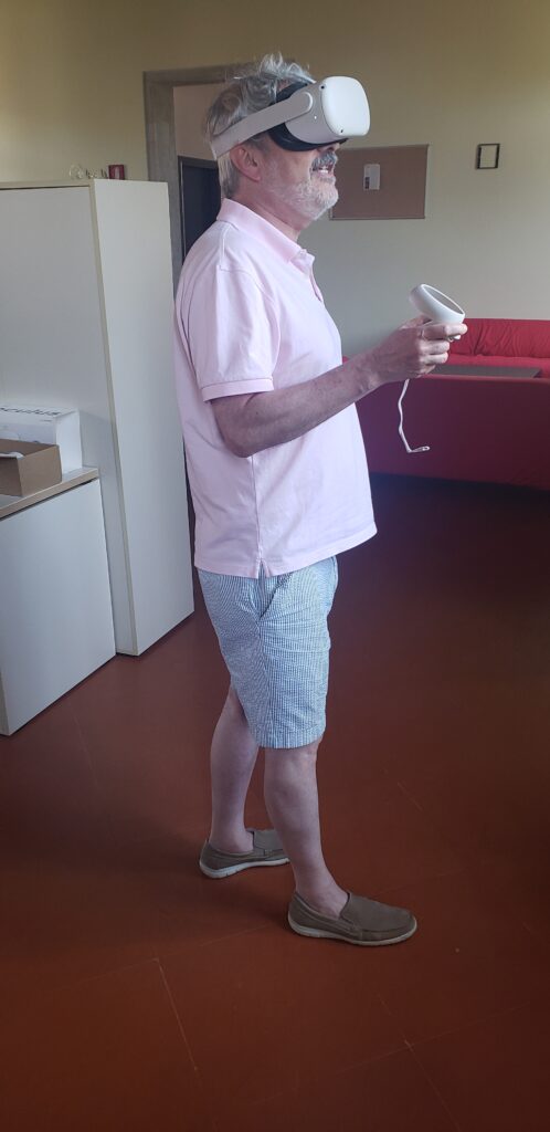A person stands wearing a VR headset and holding a hand controller.